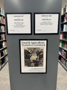 New stacks signage at Mann Library showing call number ranges, subject keywords, and a poster reading “Food & Agriculture Statistics, Livestock,” mounted on the end of a book stack between shelves of books.
